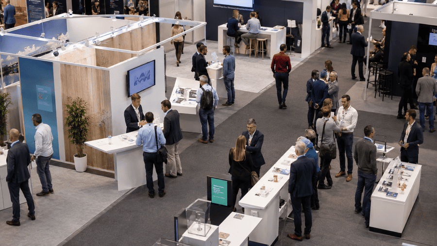 People networking at trade show stands, illustrating the value of face-to-face meetings in a digital business world.